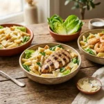 Assorted Caesar pasta salads including classic Caesar pasta salad with penne, grilled chicken Caesar pasta salad, and shrimp Caesar pasta salad on a wooden table