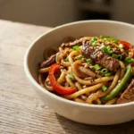 Bowl of glossy black pepper beef udon with tender beef strips, chewy noodles and colorful bell peppers