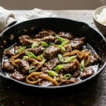 Sticky Mongolian beef and caramelized onions with sesame seeds and green onions in a black cast iron skillet
