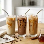 Three tall glasses of creamy protein iced coffee with ice and straws on a wooden table